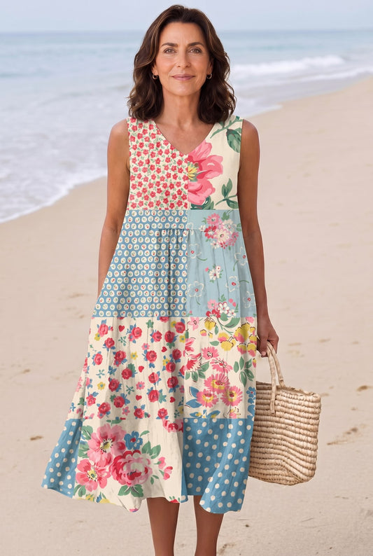 The Carolyn Resort Dress in soft floral and polka-dot patchwork (pink, blue, cream), full-length editorial on a Mediterranean beach with woven basket