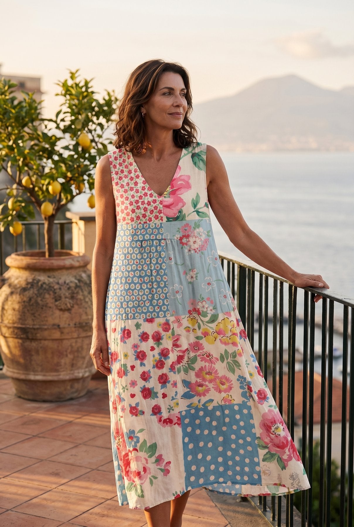 The Carolyn Resort Dress in soft floral and polka-dot patchwork, editorial full-body on a Sorrento terrace at golden hour with Bay of Naples behind