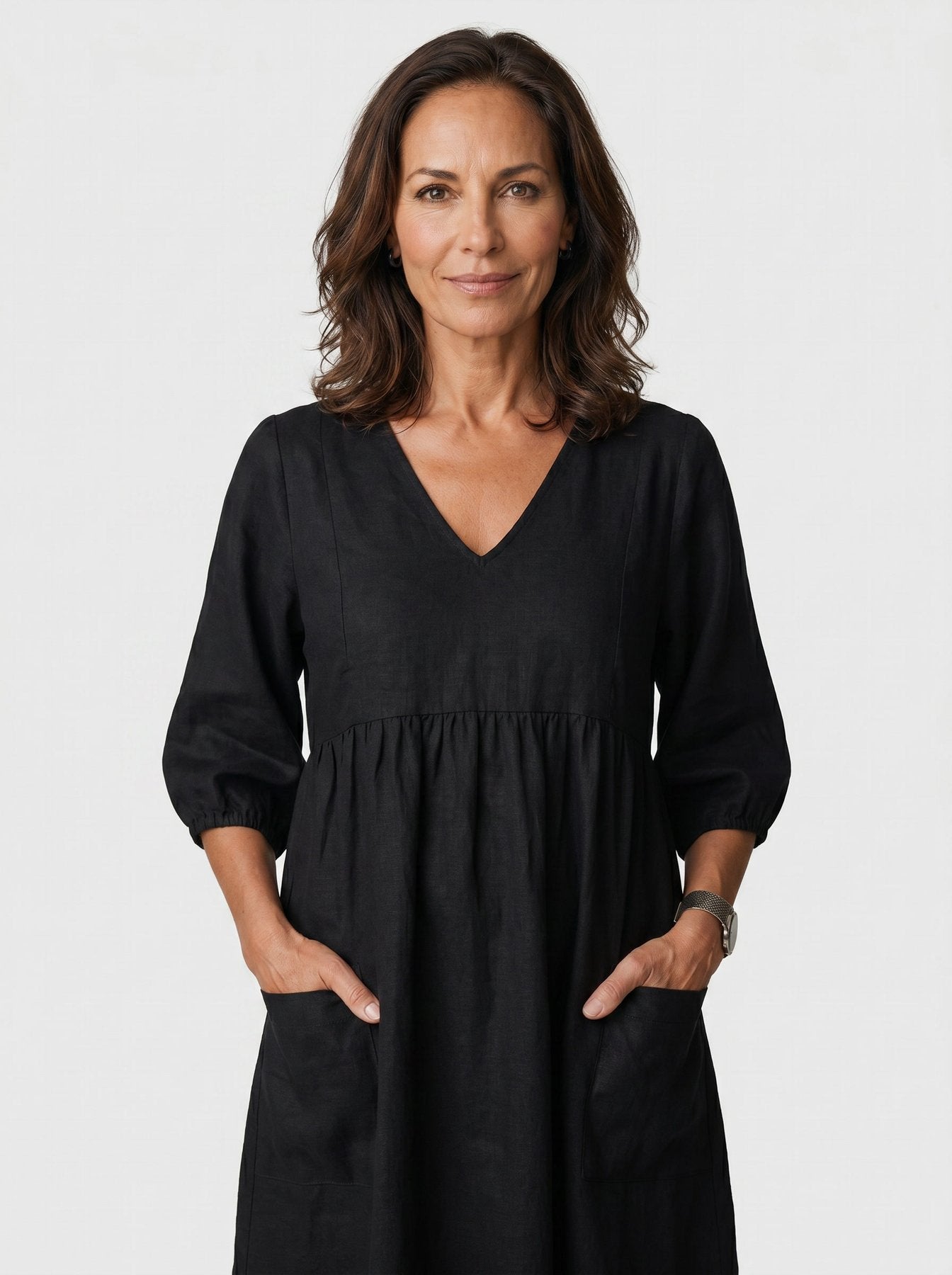 The Diane Sundress in deep black linen with V-neck and three-quarter puff sleeves, hands tucked in pockets