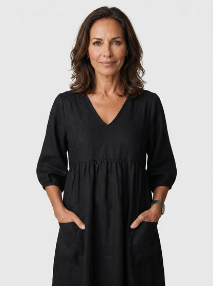 The Diane Sundress in deep black linen with V-neck and three-quarter puff sleeves, hands tucked in pockets