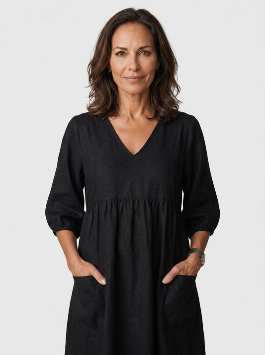 The Diane Sundress in deep black linen with V-neck and three-quarter puff sleeves, hands tucked in pockets