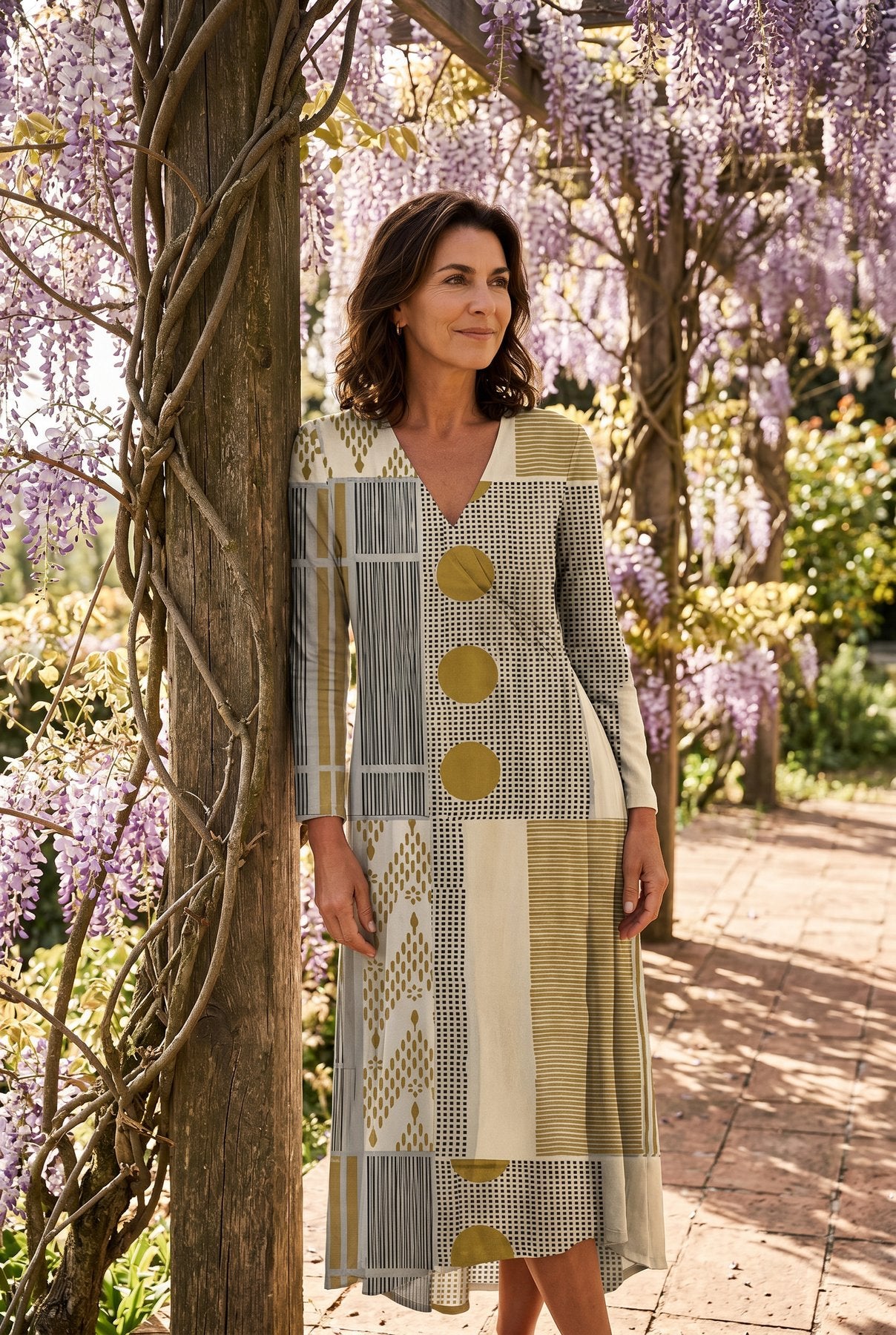 The Helen Day Dress in gray and mustard check, full-length under a wisteria pergola