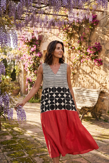 The Mary Boat Dress in stripes-and-dots, editorial full-body in a wisteria pergola courtyard with cascading purple blooms