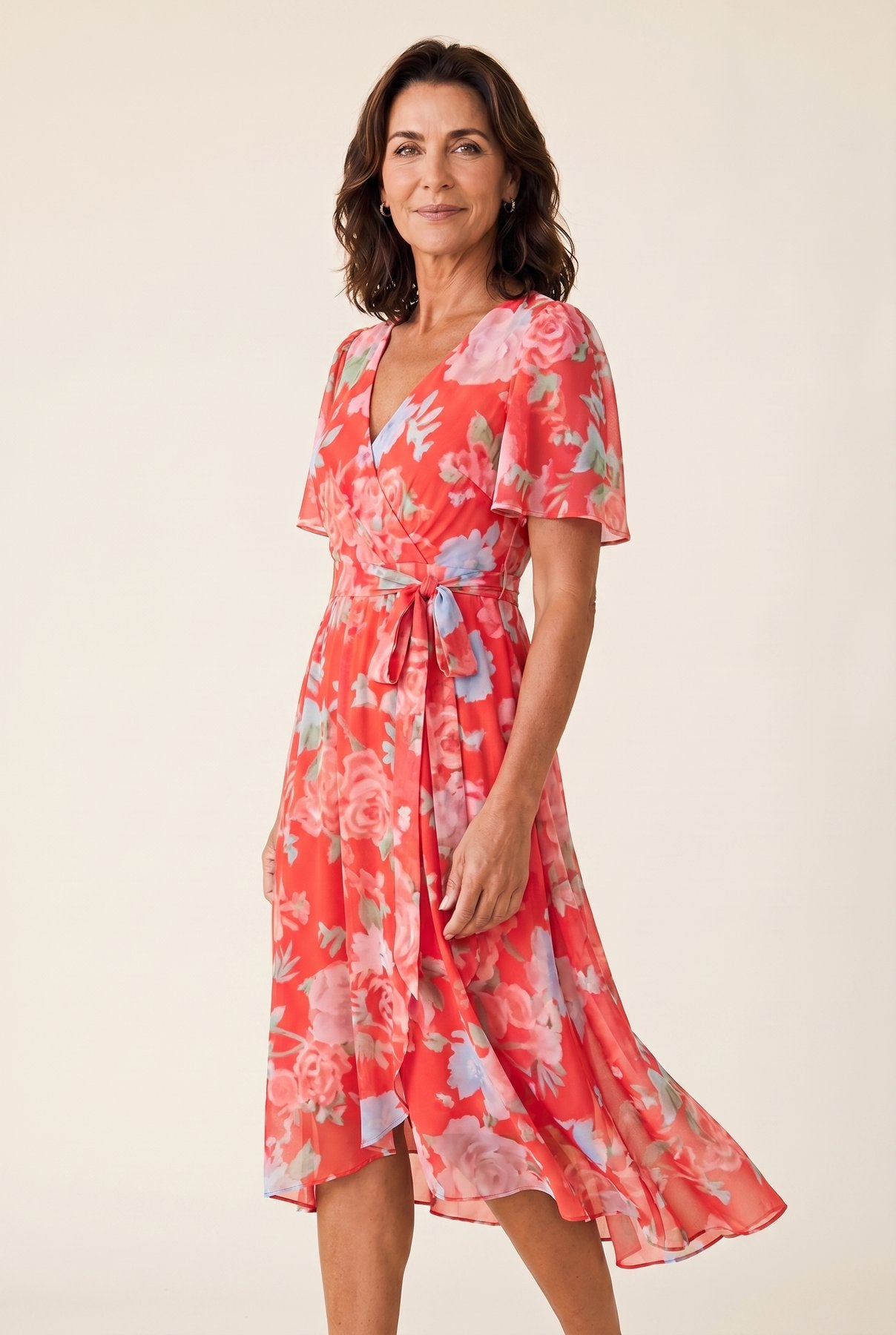 The Sandra Heat Dress in coral-pink floral colorway, chiffon V-neck wrap with flutter sleeves, cream studio editorial