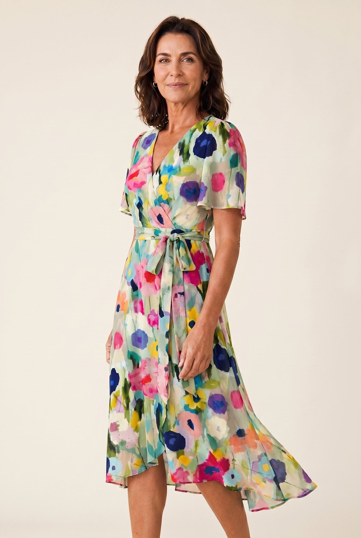 The Sandra Heat Dress in multicolor watercolor floral colorway on sage-green ground, chiffon V-neck wrap with flutter sleeves, cream studio editorial