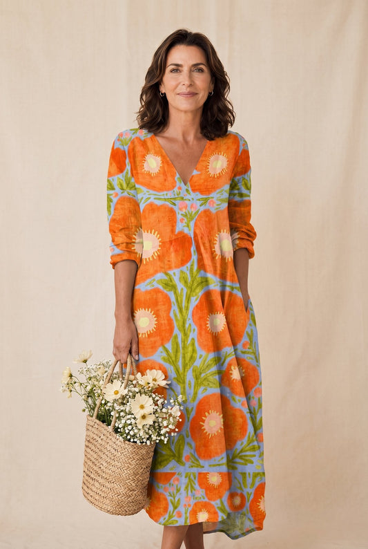 The Sylvia Cocktail Dress in orange and cream retro floral on aqua-blue, full-length editorial portrait with floral basket against a cream studio backdrop